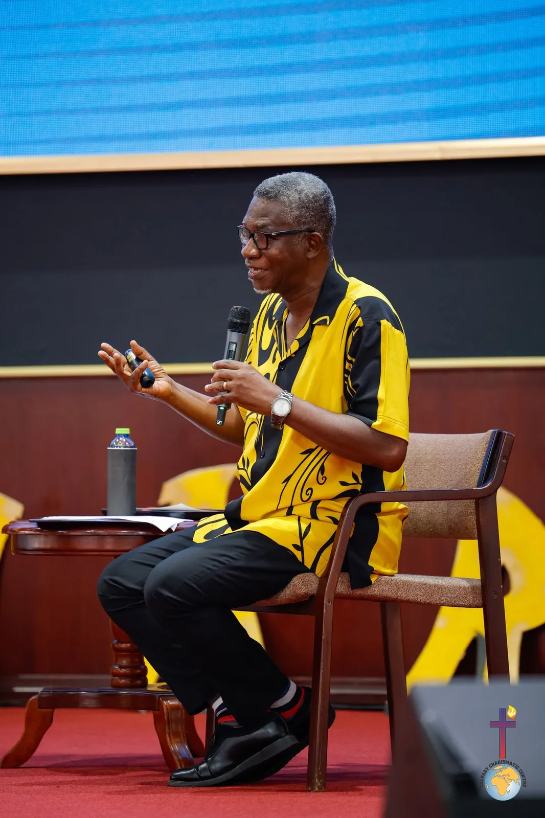 Rev. Vincent Acquaah seated on stage, explaining a point