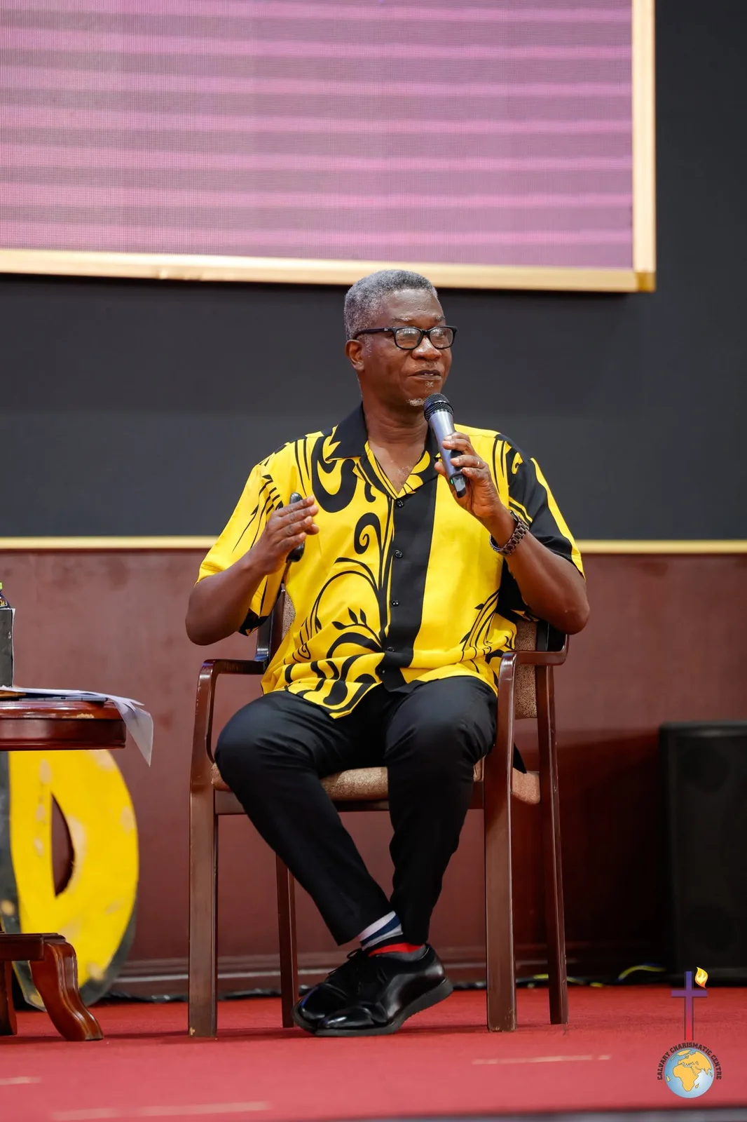 Rev. Vincent Acquaah seated and talking with a microphone