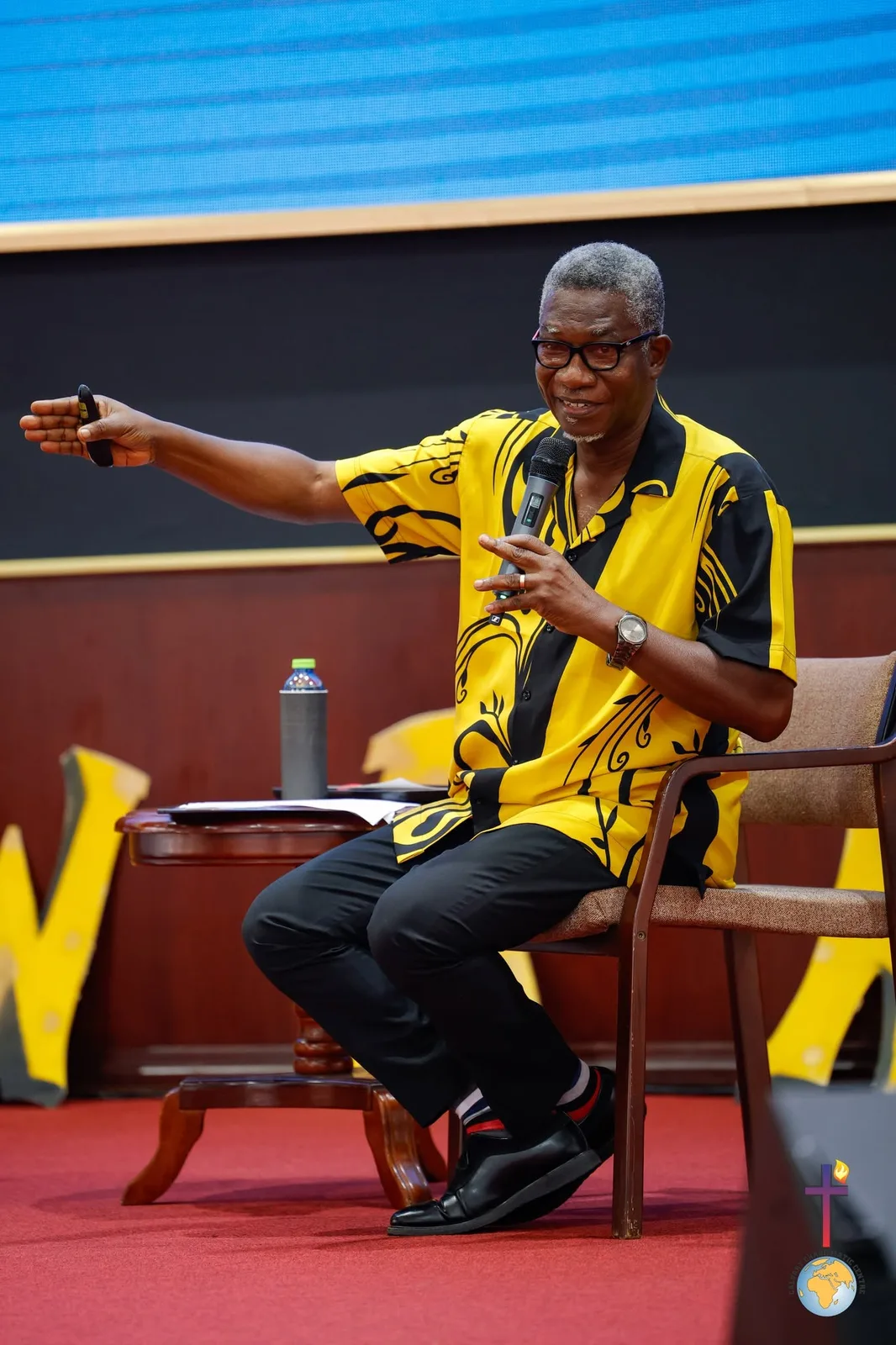 Rev. Vincent Acquaah seated on stage, pointing as he teaches